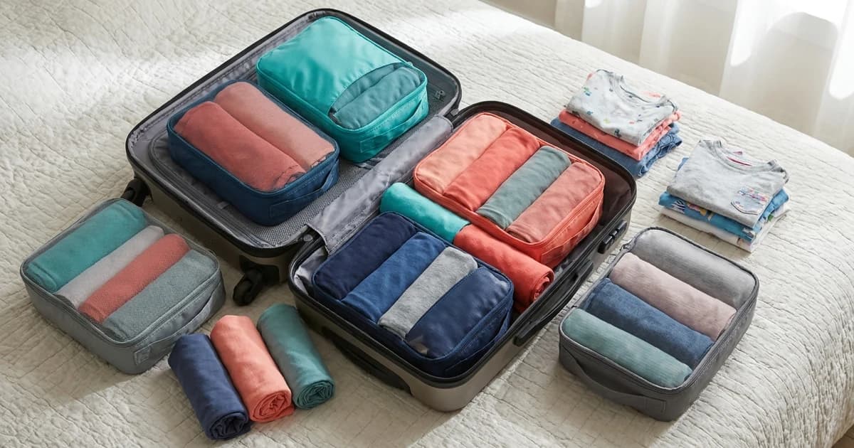 A parent and two children packing rolled clothes into colorful zippered compression packing cubes laid out on a bed before a family trip.