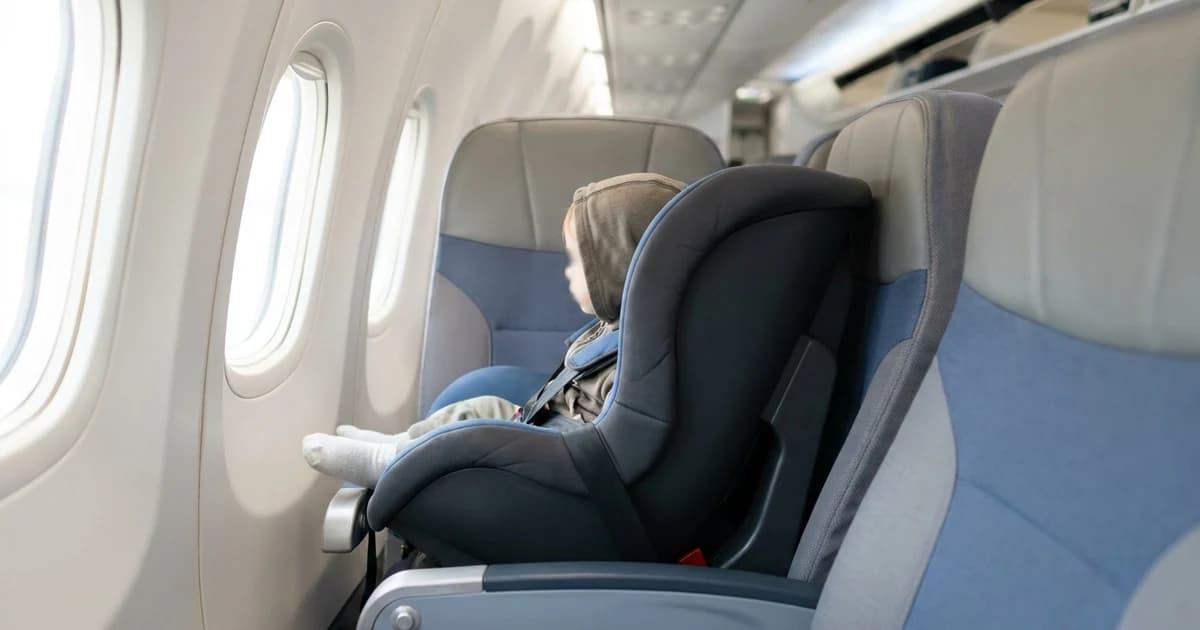 A hard-backed child car seat installed and buckled onto a window seat inside an airplane cabin