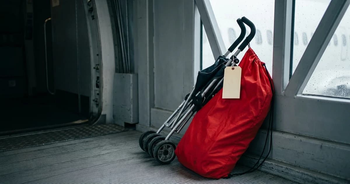 A folded lightweight baby stroller half-slipped into an open bright red gate-check bag, leaning against the wall of an airport jet bridge with a paper gate-check tag on the handlebar.