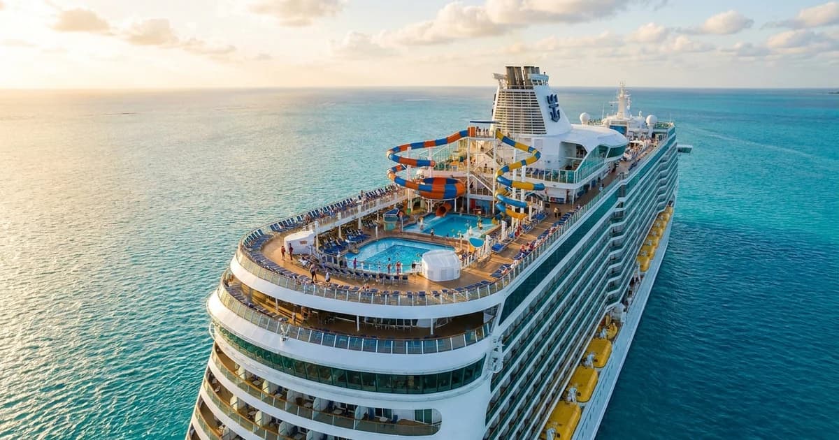 A modern family cruise ship with a pool deck and water slides sailing through turquoise tropical water under a sunny sky
