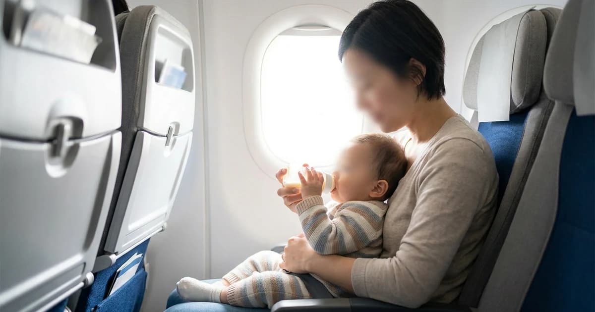 Parent helping a baby drink from a bottle in an airplane window seat during descent