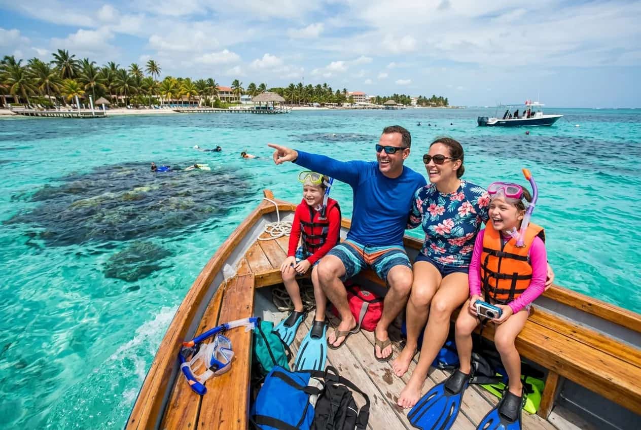 Crystal clear water over the Belize Barrier Reef with tropical fish and coral visible below a family snorkeling boat