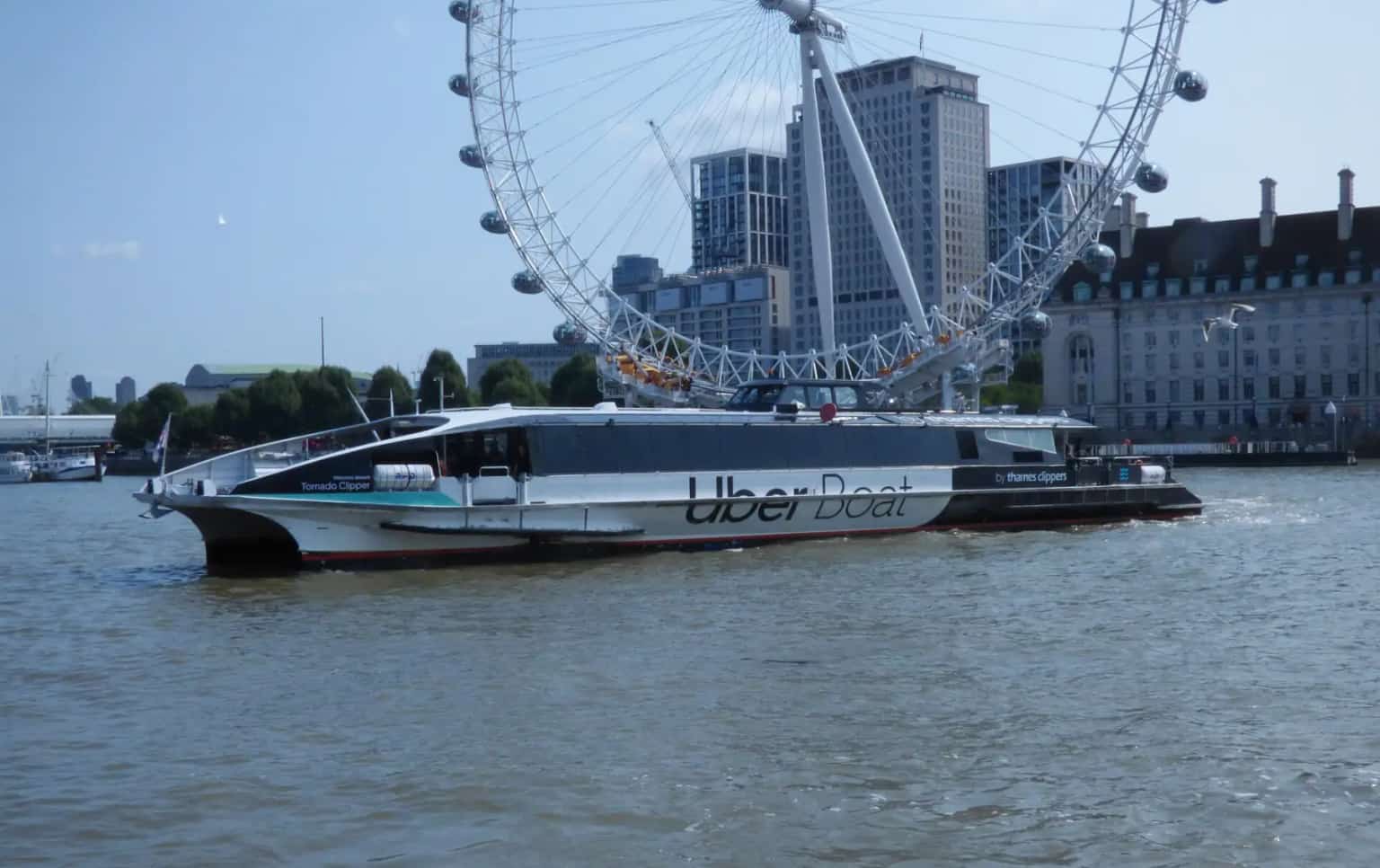 A white Uber Boat river bus on the Thames in front of the London Eye and County Hall.