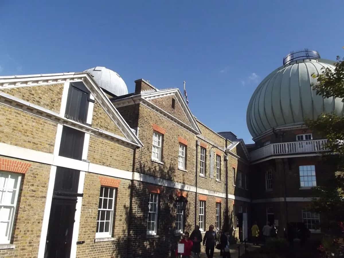 The brick Royal Observatory buildings at Greenwich with the green onion-shaped telescope dome under a blue sky.