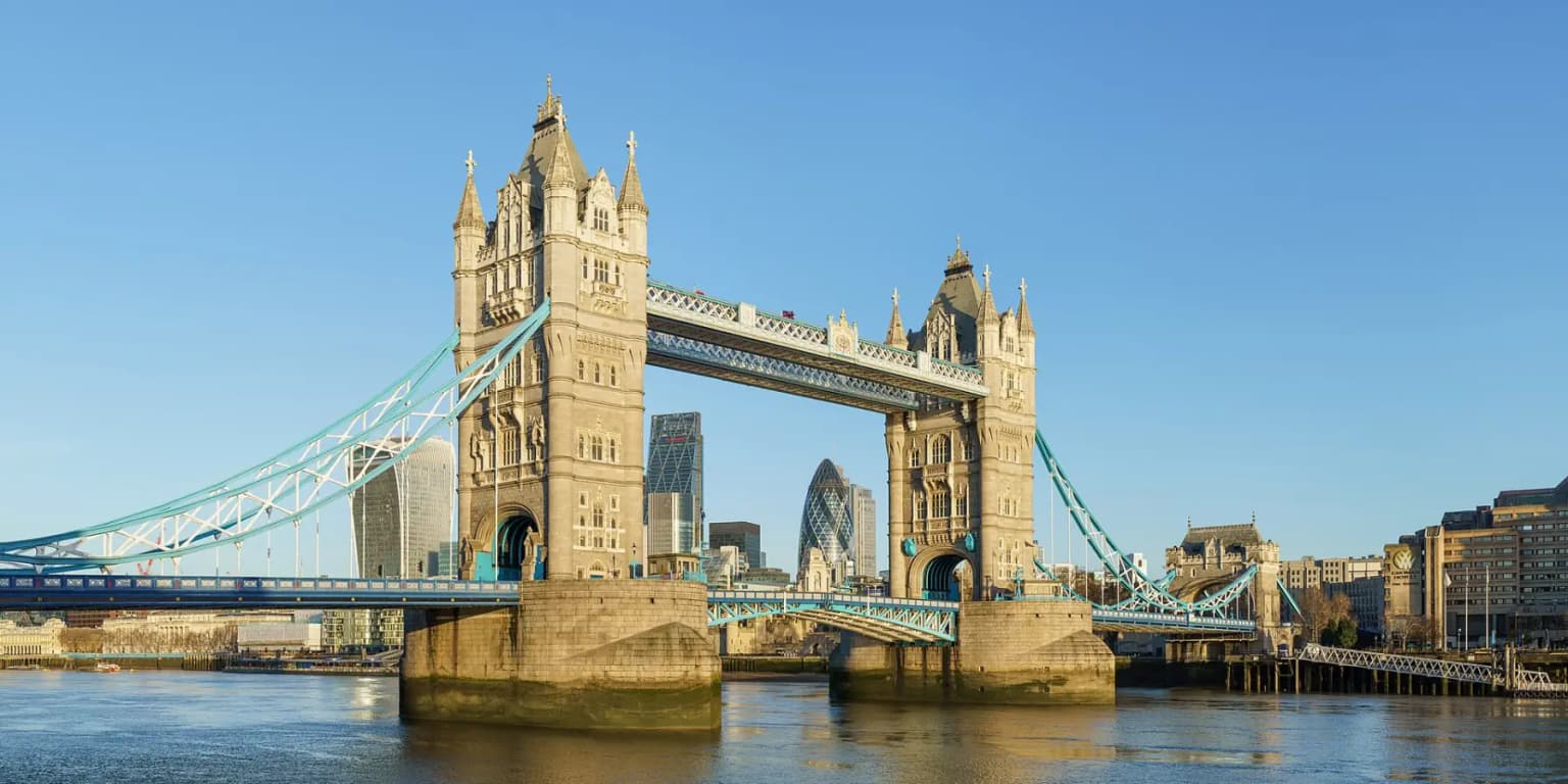 Tower Bridge over the Thames under a clear blue sky, with the City of London towers behind it.