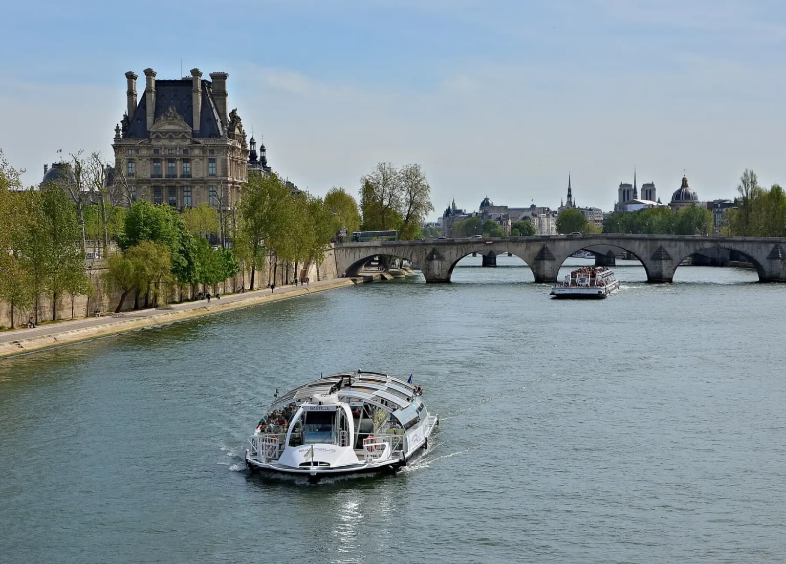 A glass-roofed Batobus river shuttle on the Seine, with the Louvre and the Pont Royal in the background.