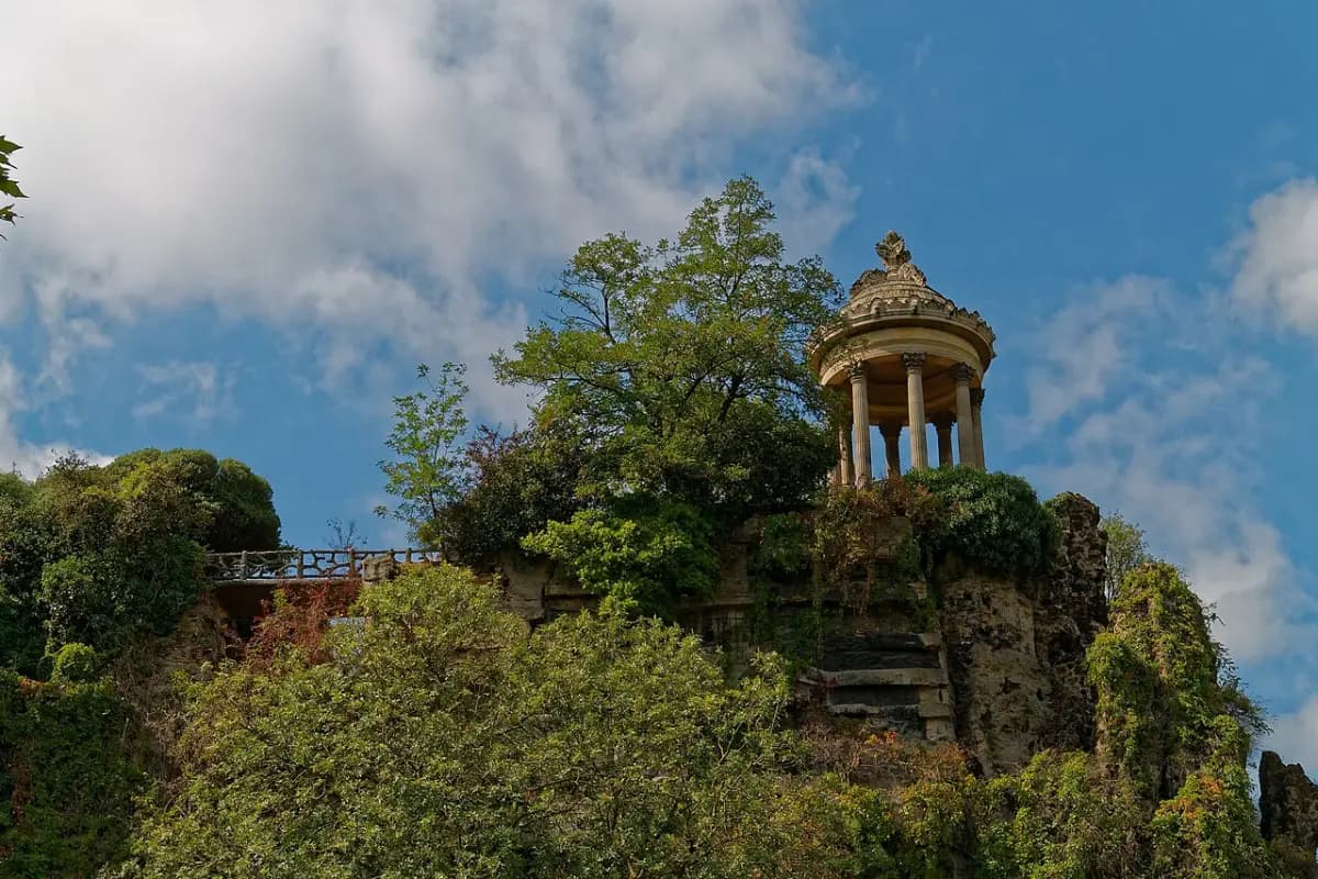 The small round Temple de la Sibylle on top of a wooded cliff in the Parc des Buttes-Chaumont under a blue sky.