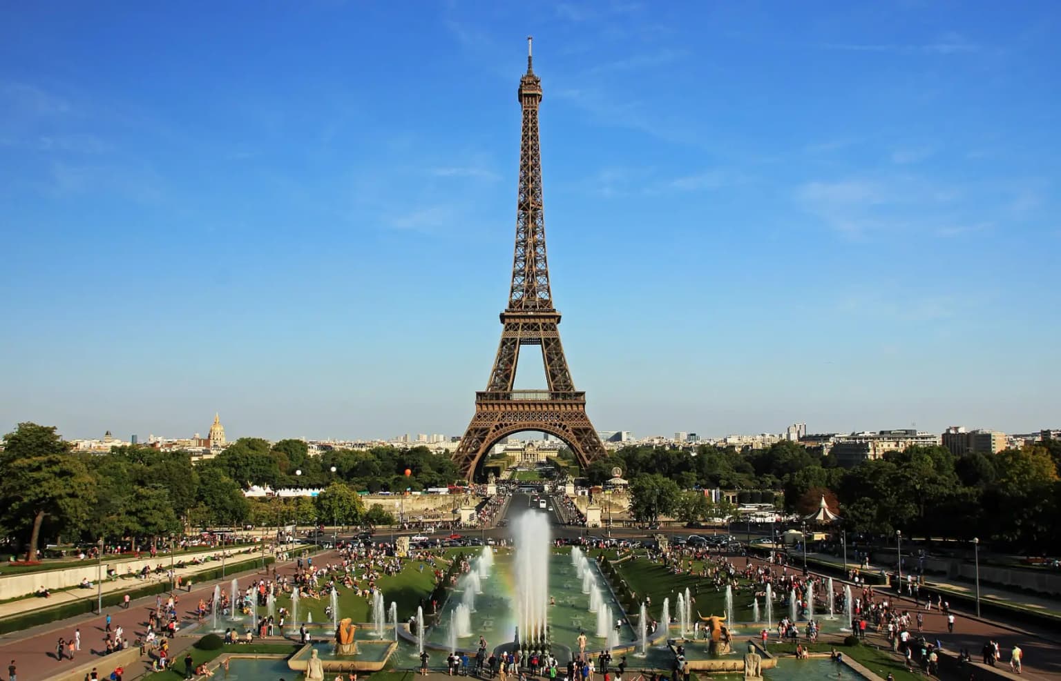The Eiffel Tower seen from the Trocadéro on a clear day, with the Warsaw fountains and crowds on the gardens in front.