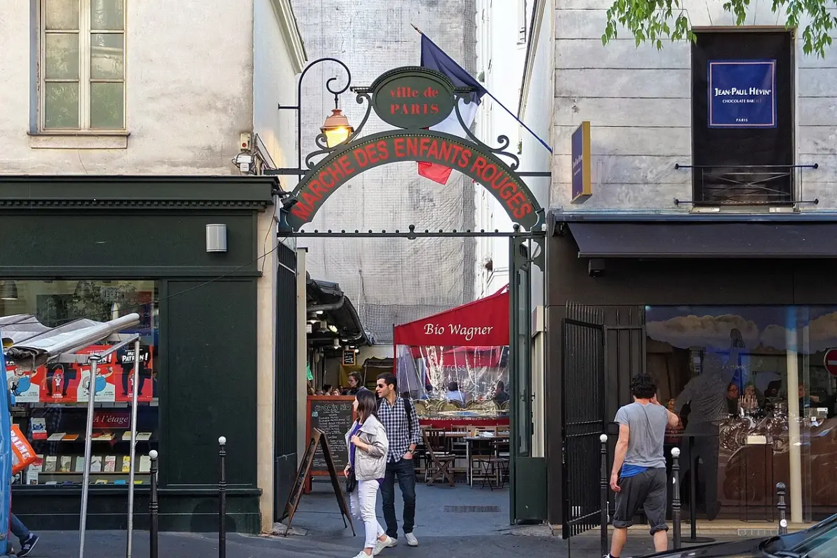 The green iron gateway and sign of the Marché des Enfants Rouges on a Marais street, with market stalls inside.