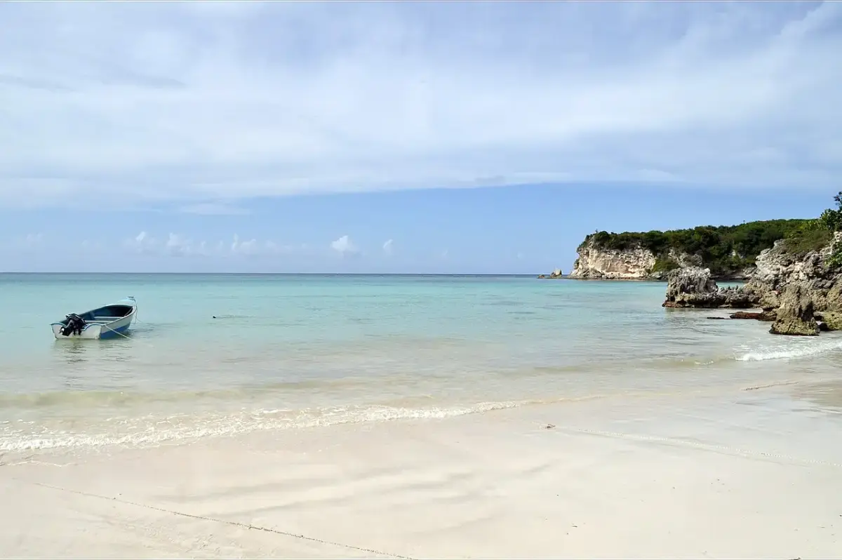 Pale sand and clear water at Playa Macao with a small boat and a rocky headland