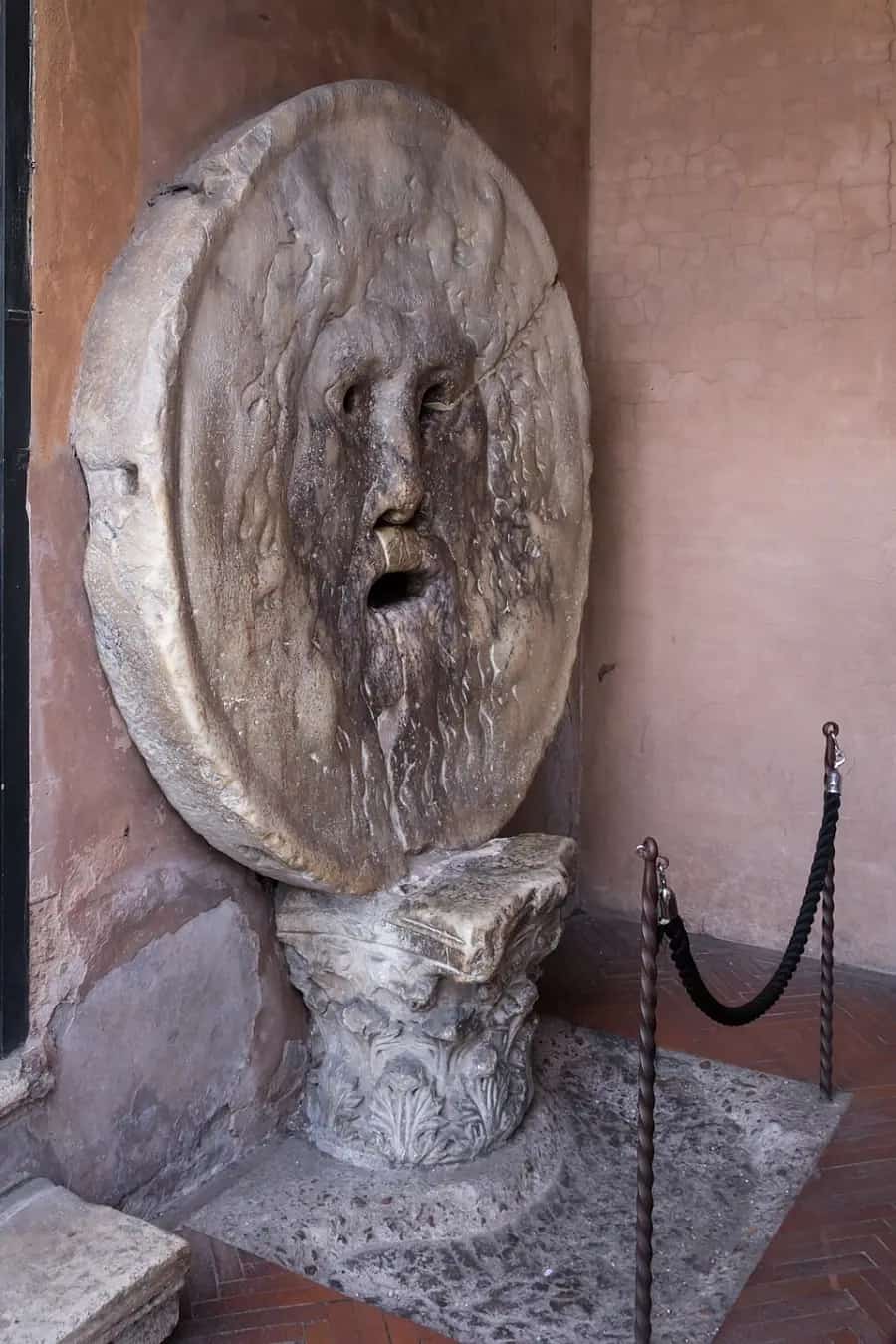 The Mouth of Truth, a round marble mask with an open mouth, against the wall of a church portico.