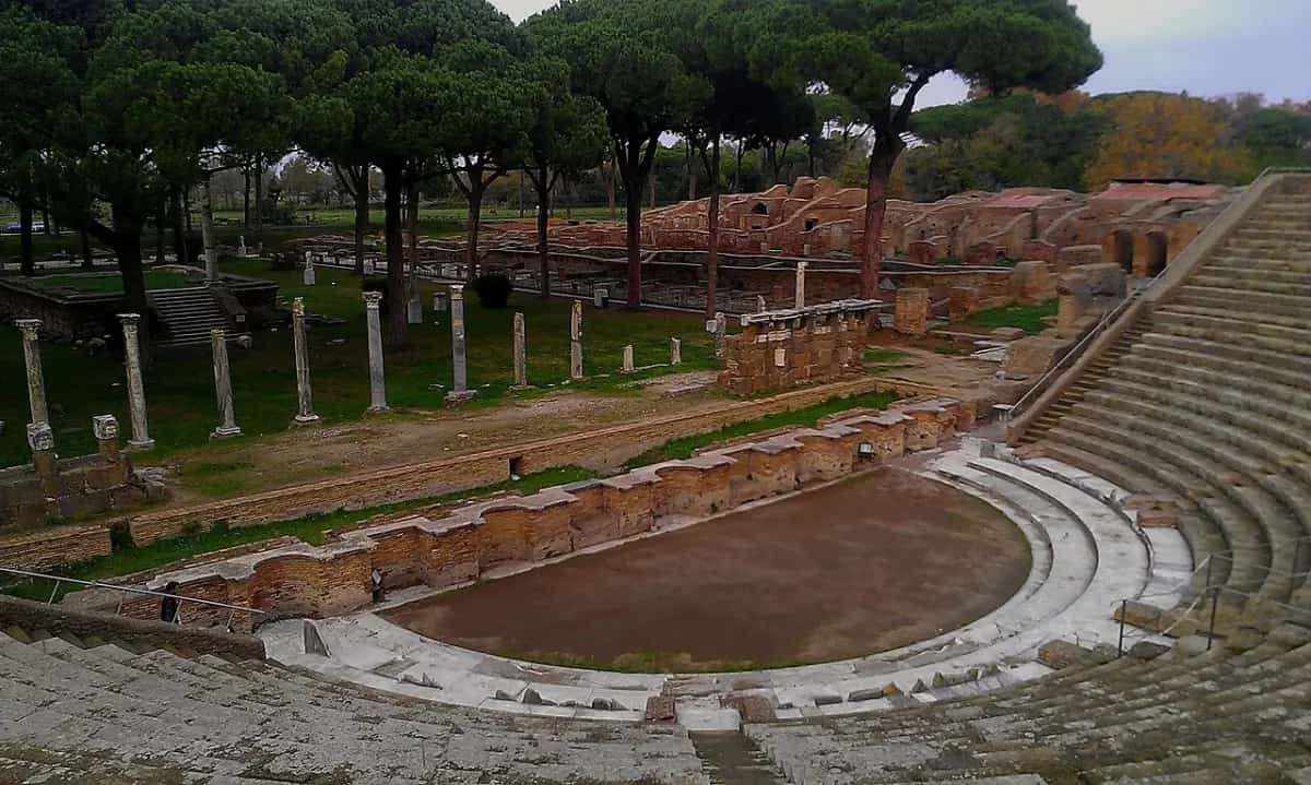 The curved stone seating of the Roman theatre at Ostia Antica, surrounded by umbrella pines.