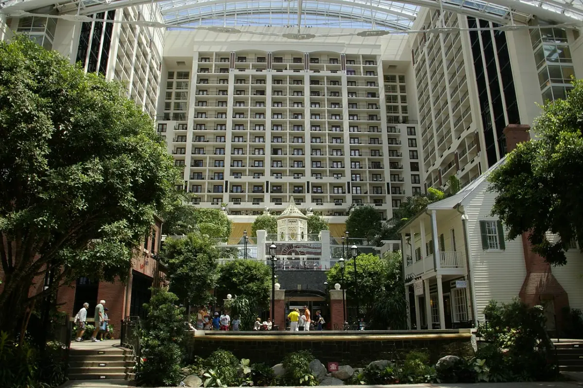 The Gaylord National's glass-roofed atrium with trees, garden paths and a tall wall of hotel room balconies behind.