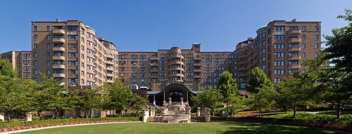 The long brick Omni Shoreham Hotel with its wings and gardens, seen across a lawn on a sunny summer morning.