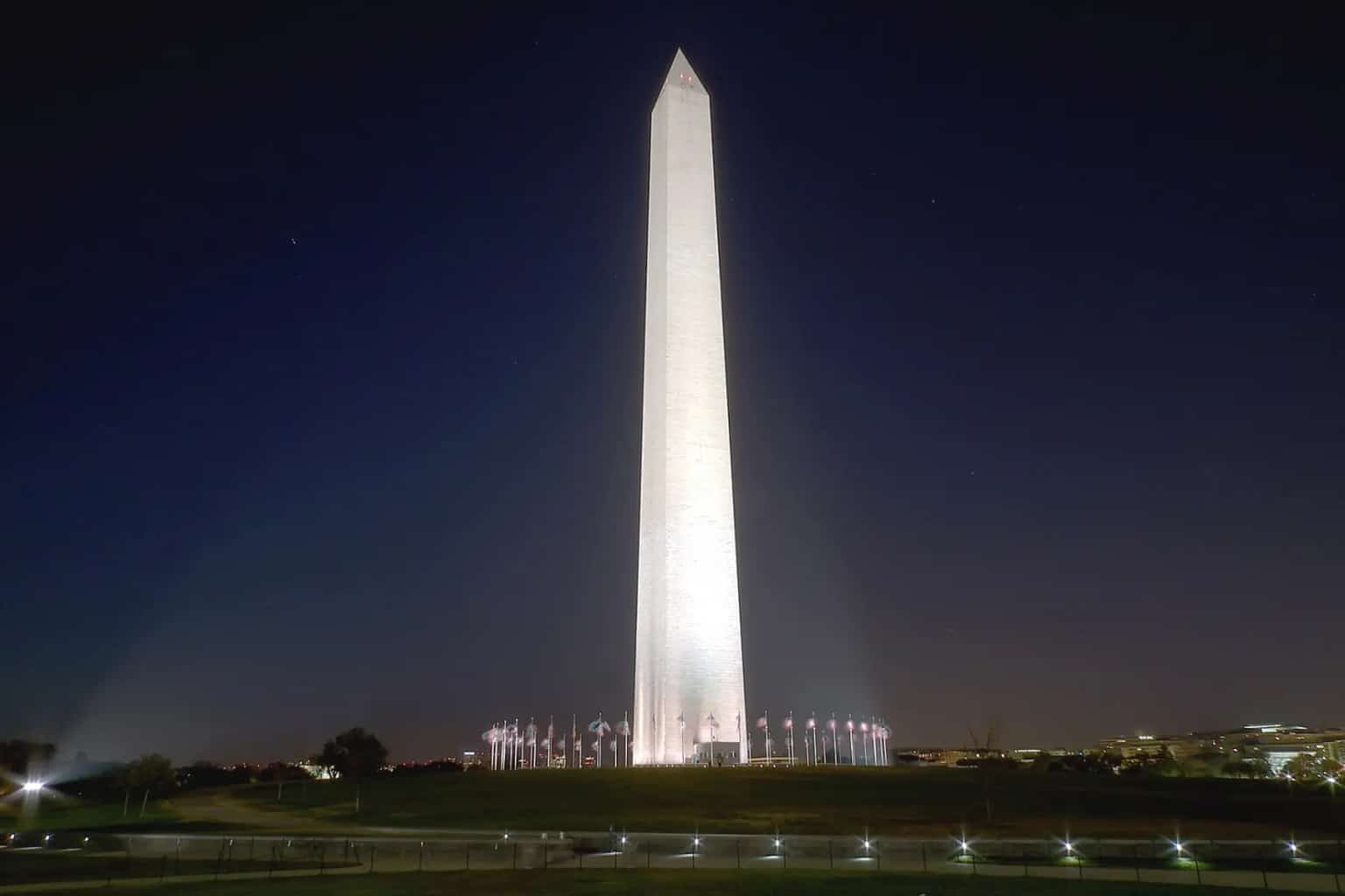 The Washington Monument floodlit against a dark early-morning sky, with lights along the base.