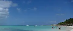 Wide shallow turquoise water off Playa Norte with swimmers standing far from shore and boats beyond