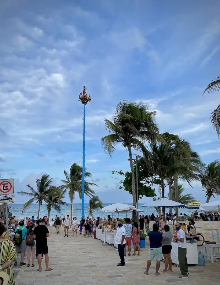 Voladores ceremony pole with performers at the top against a blue sky and palm trees in Playa del Carmen