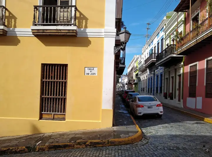 A yellow colonial building on a corner of a cobbled Old San Juan street lined with colourful houses