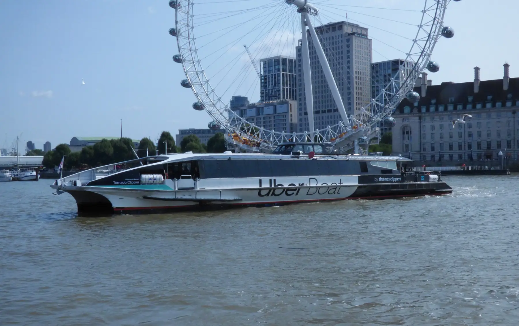 A white Uber Boat river bus on the Thames in front of the London Eye and County Hall.