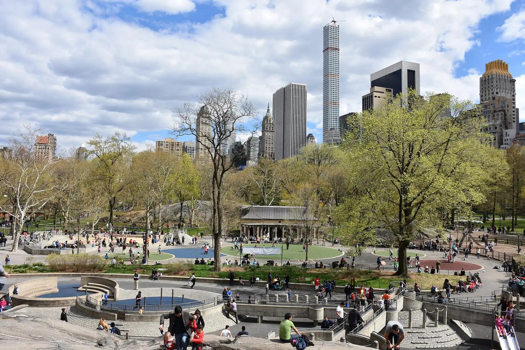 Heckscher Playground in Central Park from Rat Rock, with play structures, families and the Central Park South skyline under a blue sky.