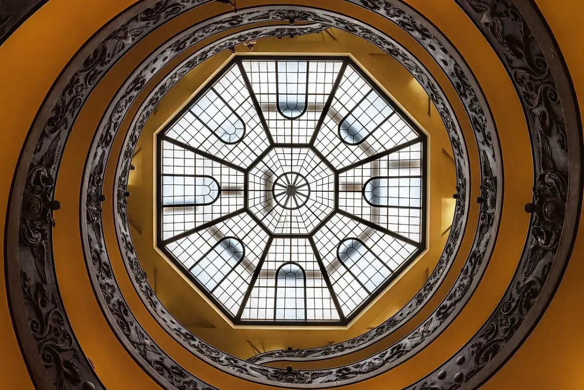The double spiral staircase at the Vatican Museums seen from the bottom, coiling up toward a glass dome.